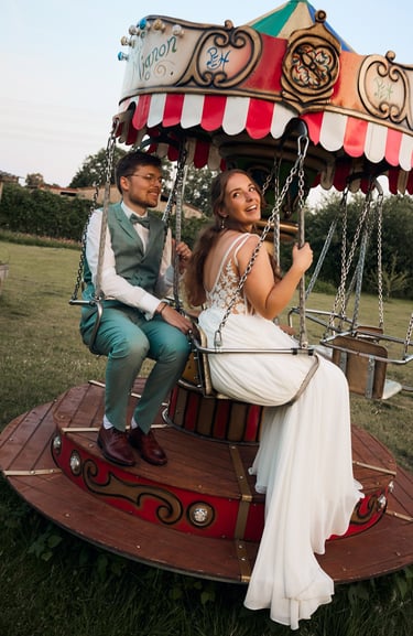 A happy bride and groom enjoying a ride on a vintage carnival carousel at their outdoor wedding.