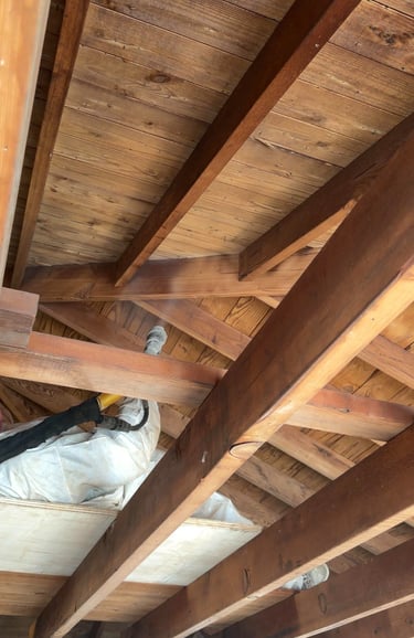 A worker in a white suit using a dry ice blaster to restore wood ceiling beams in an attic.