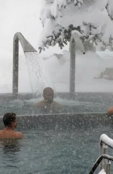 Close-up of people relaxing under a warm waterfall massage in an outdoor hot spring while it is snow