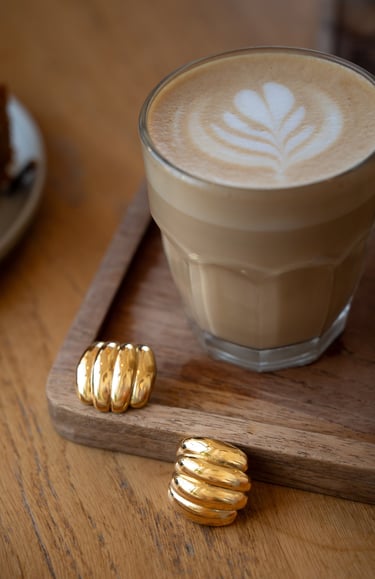 gold jewelries and a cup of coffee with a piece of cake on a tray