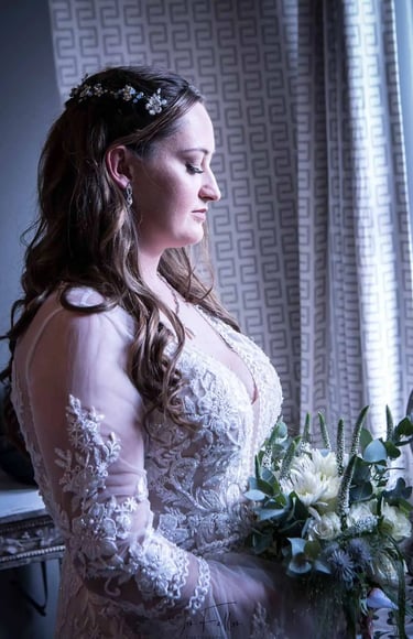 Side profile of a bride in an embroidered lace wedding dress holding a white floral bouquet.