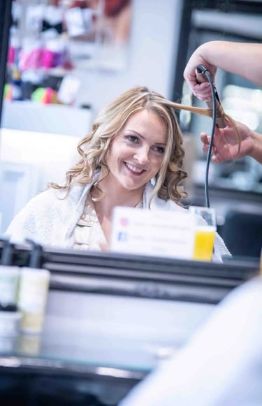 Smiling woman getting her blonde hair curled with a styling iron at a professional hair salon.