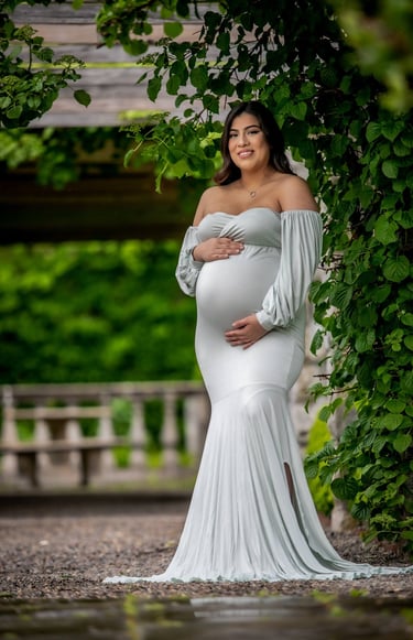 a pregnant woman in a white dress standing in front of a tree