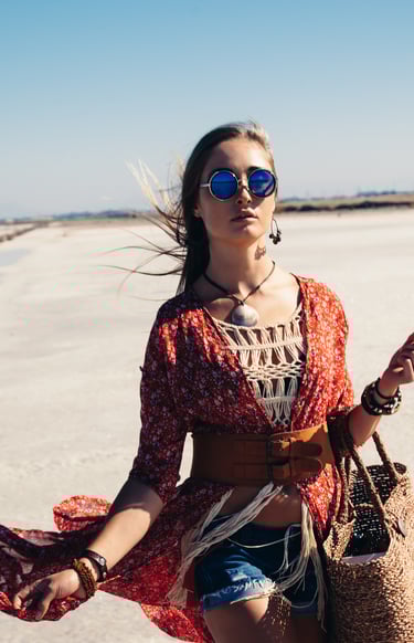 a woman in a red dress and sunglasses walking on a beach