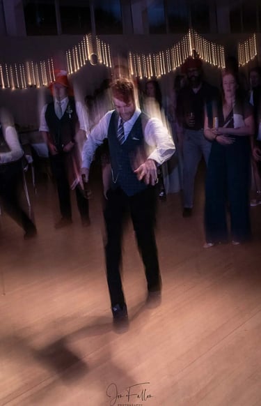 A groom dancing on a wooden dance floor during a wedding reception with motion blur and fairy lights.