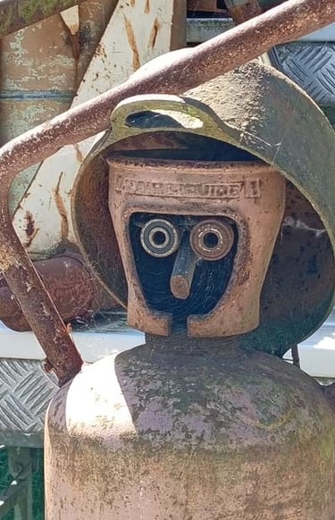 Rusty vintage gas cylinder modified into a scrap metal sculpture of a human face with a helmet.