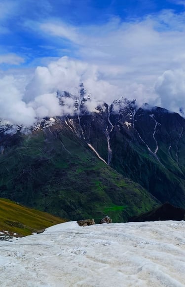 Snowy peaks with clouds over green valleys.