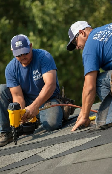Professional roofing contractors installing asphalt shingles on a residential roof using a pneumatic nail gun.