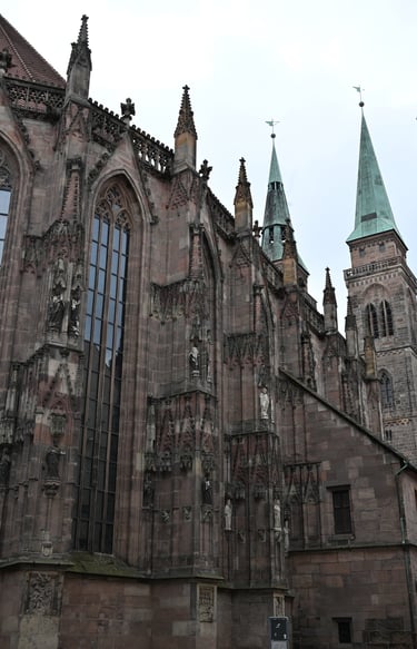 Gothic architecture of St. Sebaldus Church in Nuremberg featuring ornate stone carvings and green spires.
