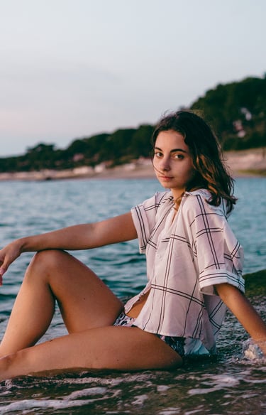 femme assise sur la plage portant une chemise et un maillot de bain regardant l'objectif
