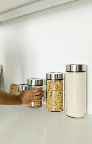 A person reaches for glass kitchen storage jars filled with almonds and cereal on a white counter.