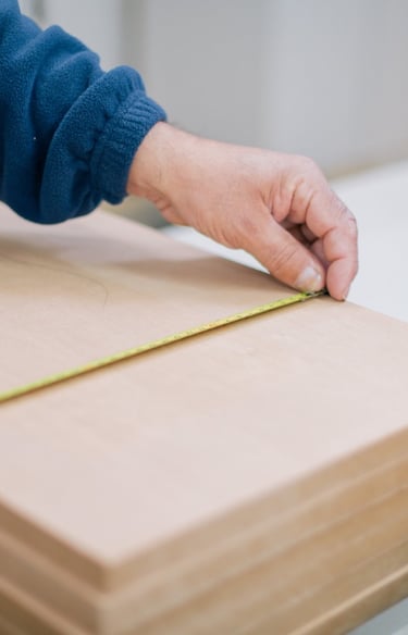 Mano midiendo tabla de madera con cinta métrica.
