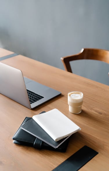 An open laptop, datebook, notebook, and coffee cup on top or a wodd desk.