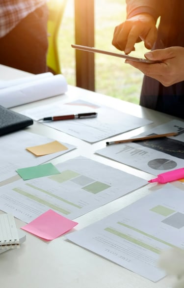 Project charts spread out on a desk with Post-It Notes and markets