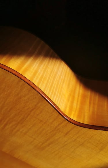 Close-up of a acoustic guitar with a natural flamed maple wood, and french finish and dark binding.