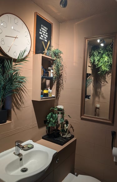 Modern bathroom decor featuring a wall clock, vanity mirror, and lush green indoor plants.