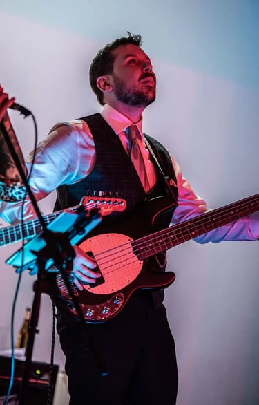 Groom plays a black electric bass guitar on stage with red and blue lighting.