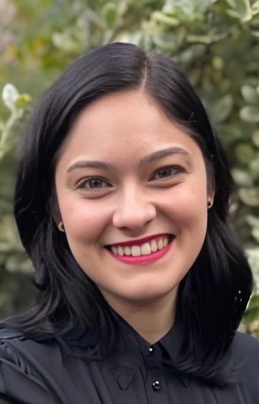Smiling woman with black hair and red lipstick posing against a blurred green garden background.