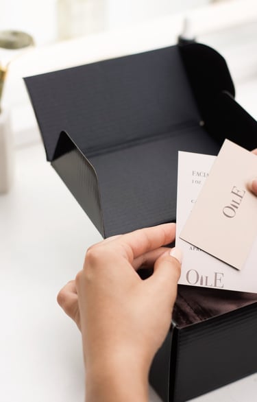 Hands opening a black luxury skincare gift box with Oile brand facial product cards.