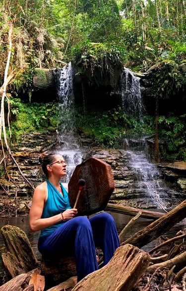 a woman sitting on a log in the woods infront of a waterfall