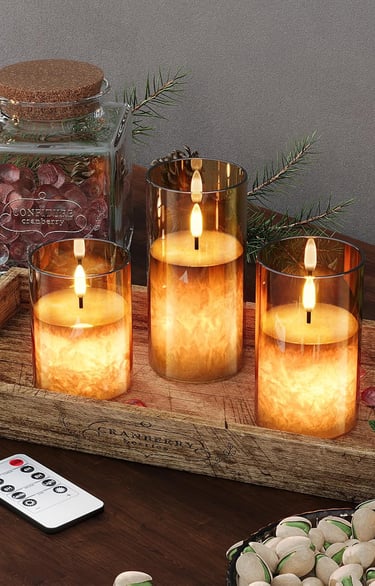 Three flameless LED glass pillar candles with remote control on a rustic wooden tray.