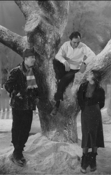 Berkeley sitting in a snowy prop tree, directing Ruby Keeler and Dick Powell on a winter set.