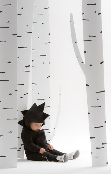 Fashion campaign photography - a baby in a black dinosaur outfit sitting by trees