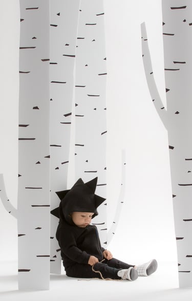 Fashion campaign photography - a baby in a black dinosaur outfit sitting by trees