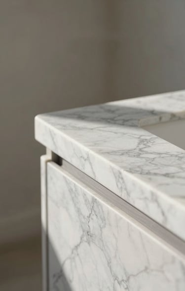 A tight, high-contrast portrait shot of natural morning daylight catching the clean, polished edge of a Carrara marble countertop against a soft neutral background.