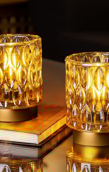 Two amber glass hurricane candle holders with decorative textured patterns glowing on a table.