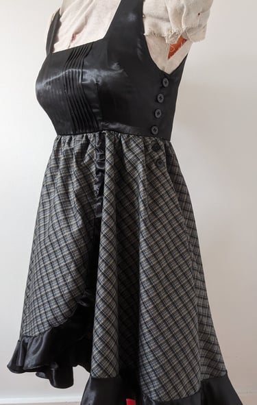 The side of a black/gold plaid and black satin flowy cocktail dress
