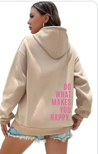 A woman wearing a beige oversized hoodie with pink text that reads Do What Makes You Happy on the back.