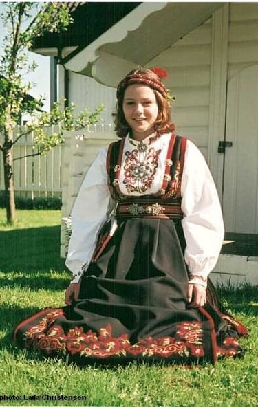 A girl sits in the grass wearing a bunad and head piece