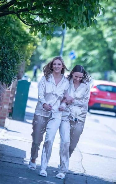 Two happy women walking on a city sidewalk wearing matching silk pajamas and slippers.