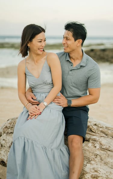 Parents sharing a relaxed moment by the shoreline during a family photography session at The Ritz-Carlton Bali.