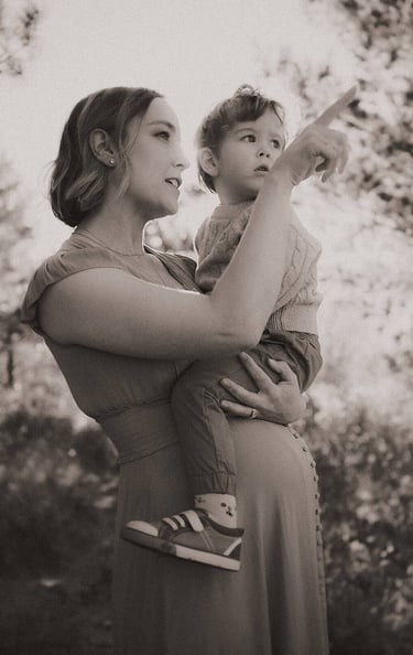 Pregnant mom holding toddler, both pointing and looking into the distance.