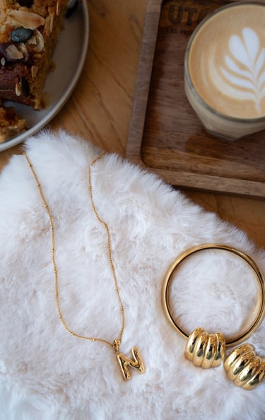 gold jewelries and a plate with a cup of coffee and a plate with a cake