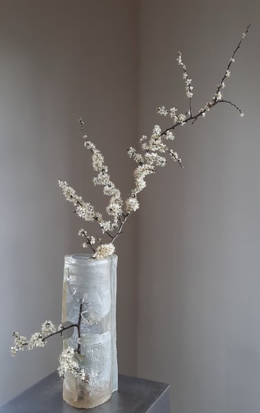 an icy glass vase with a flowering branche in it.