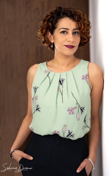 a woman in a green blouse and black pants leaning against a wall