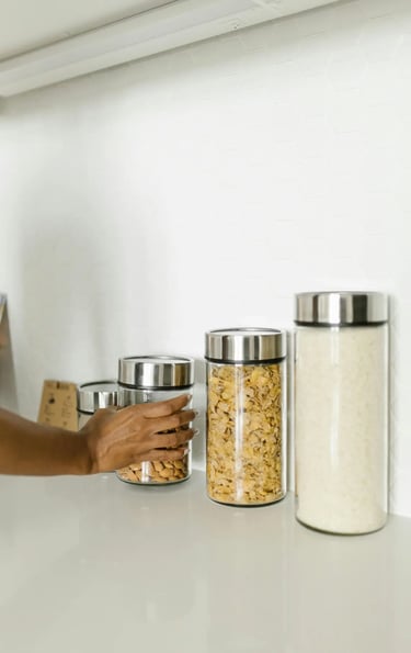 A person reaches for glass kitchen storage jars filled with almonds and cereal on a white counter.