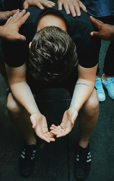 a man sitting on a chair with his hands on his knees and people praying for him