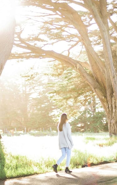 a woman walking down a path with trees in the background