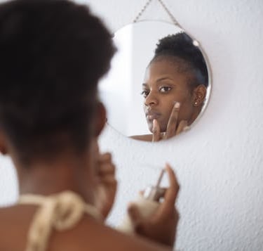dark skin lady looking in mirror putting cream on spot