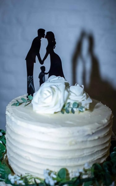 White tiered wedding cake with white roses and a silhouette cake topper of a bride, groom, and child.