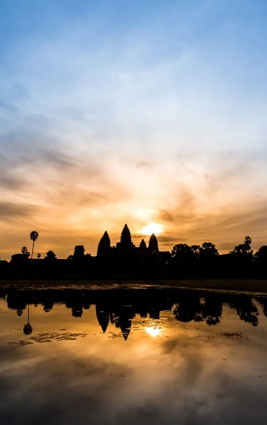 Angkor Wat temple silhouette at sunrise with dramatic orange sky and palm trees reflected in still w