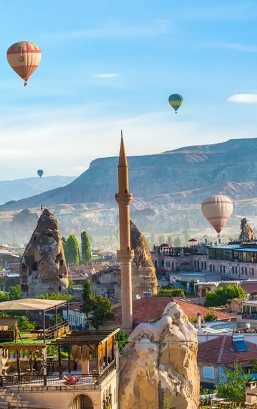 Colorful hot air balloons flying over Cappadocia town with fairy chimneys, mosque minaret, and rocky