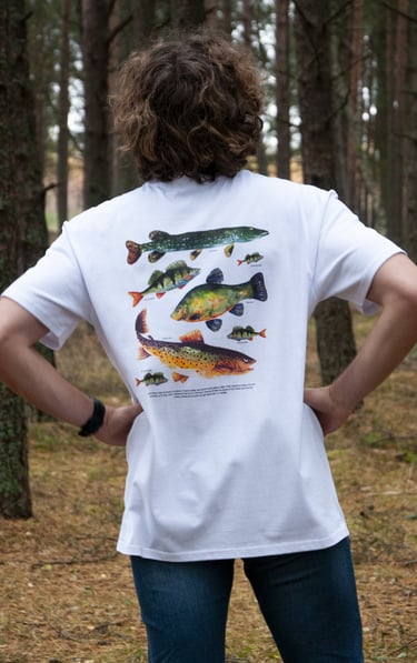 a man in a white shirt with handdrawn fish illustation and jeans standing in front of a forest