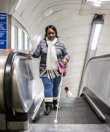 Woman using a cane while getting off an escalator, demonstrating mobility for the visually impaired.