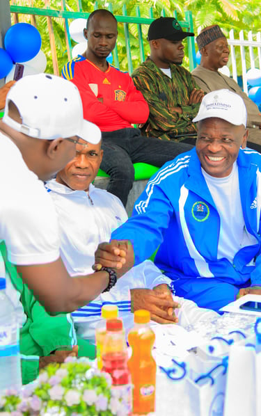 a man in a blue jacket and white shirt sitting at a table with balloons