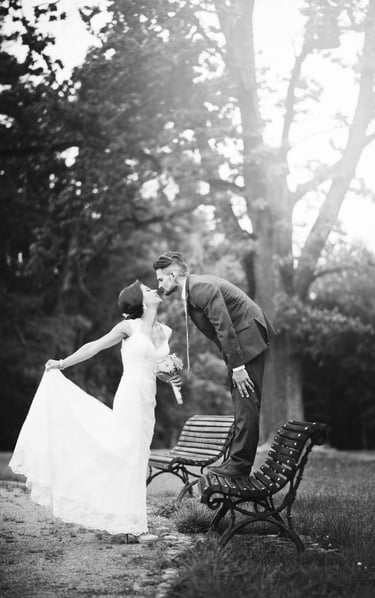 a bride and groom kissing on a bench in a park